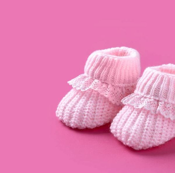 Pink knitted baby booties on a pink background.