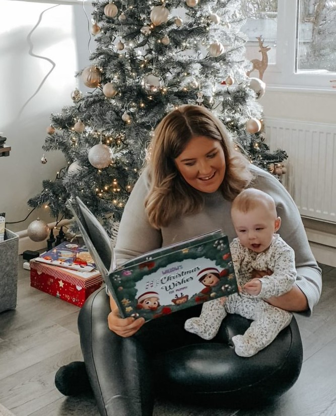 A mother and child read a personalised xmas book together next to a Christmas tree.