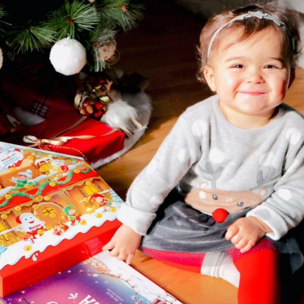 A little girl smiles after receiving a personalised christmas book as an xmas gift.