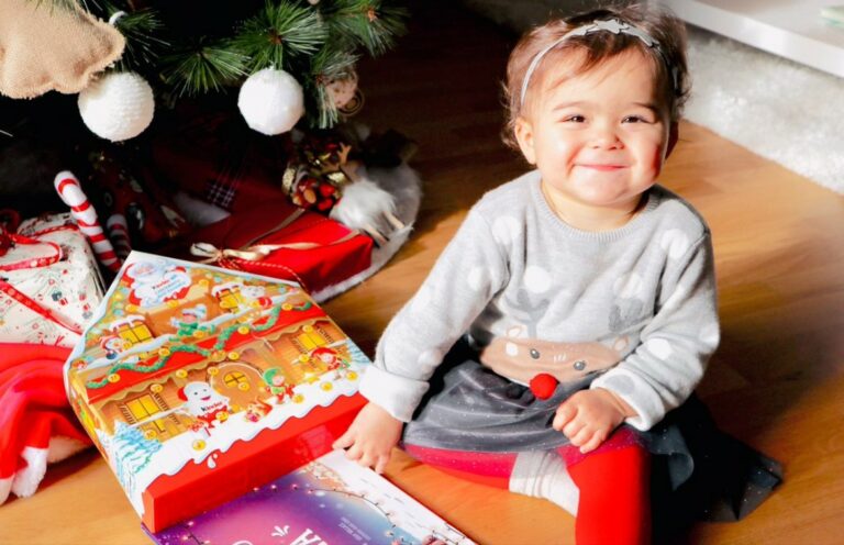 A little girl smiles after receiving a personalised christmas book as an xmas gift.