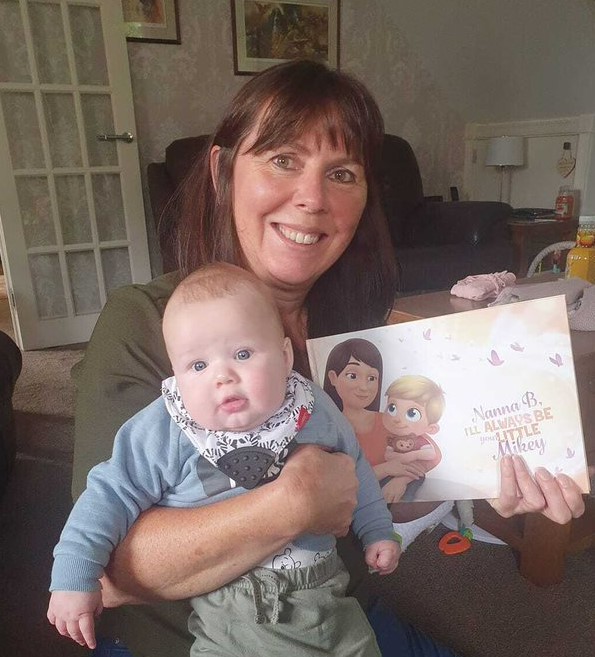 Nan cuddles her baby grandson in one hand as she holds a personalized book for grandmothers in the other.